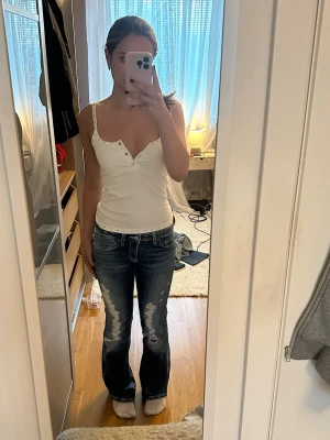 Blå slitna bootcut jeans - Säljer ett par blå bootcut jeans med slitningar framtill och lätt tvättad look. Jeansen har låg midja och klassiska fem fickor. Perfekta för en avslappnad och trendig stil. Inget synligt märke men riktigt snygga detaljer och skön passform.