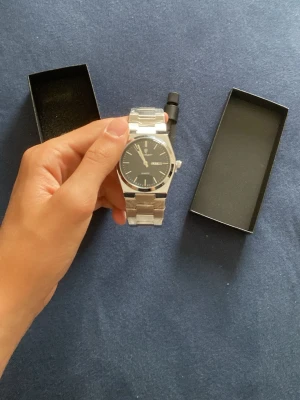 Stilren silverfärgad klocka från poedagar. - Snygg klocka med svart urtavla och silverfärgad länk i metall. Klassisk design med tydliga markeringar och datumvisning. Perfekt accessoar för dig som gillar en clean och tidlös look. Levereras i originalask. Justerare medföljer.