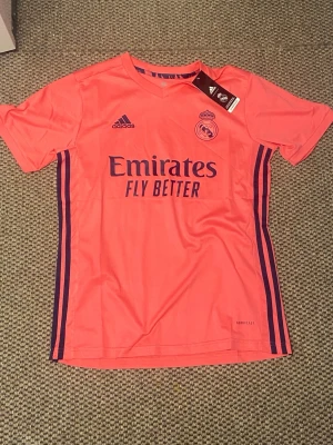 Real Madrid rosa matchtröja Adidas - Säljer en rosa Real Madrid matchtröja från Adidas med mörkblå detaljer och logga på bröstet. Tröjan har korta ärmar, rund hals och är tillverkad i lätt funktionsmaterial. Perfekt för fotbollsträning eller som supporterplagg.