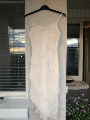 Vit långklänning med volanger - Säljer en elegant vit långklänning med tunna axelband och volangdetaljer längs hela klänningen. Jätte fin nu under sommaren.  Formar kroppen jätte fint som ett timglas, säljer även en likadan klänning i rött. Pris går att diskutera 💕