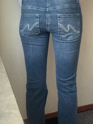 Nelly lågmidjade Y2K jeans med broderade fickor (Nyskick!) - Snygga blå bootcut jeans med ljusa kontrastsömmar och dekorativa bakfickor. Klassisk femficksmodell i stretchigt denimtyg som sitter tajt över låren och släpper ut vid vaden. Perfekta för en avslappnad och trendig look.