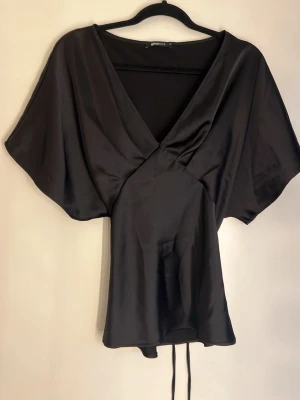 Blus - Svart satinblus med v-ringning och knytning bak. 