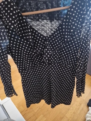Svart prickig blus med volang - Svart blus från Lindex med vita prickar, v-ringning och volangdetaljer. Perfekt för dig som gillar en lekfull och trendig stil.