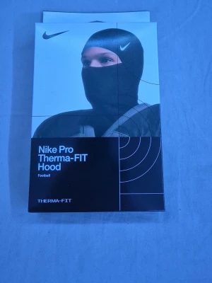 Nike Pro Therma-FIT Hood svart - Nike mask i svart, tight och sportig huva i funktionsmaterial som håller dig varm under träning eller match. Perfekt för fotboll eller annan utomhussport. Snygg Nike-logga och Therma-FIT-teknologi för extra värme