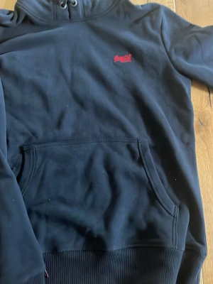 Mörkblå hoodie från Superdry - Mörkblå hoodie från Superdry, väldigt fin och aldrig använd. Fick den i julklapp och drog av prislappen. Aldrig använd alldrig tvättat allt är nytt👍 fkn basic superdry hoodie med fin marinblå färg. Priset är inte hugget i sten 🪨 