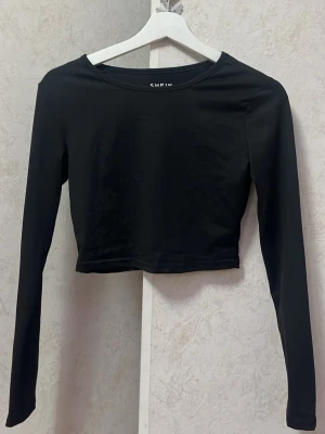 Svart croppad långärmad topp SHEIN - Snygg svart croppad långärmad topp från SHEIN. Tillverkad i mjukt material som sitter skönt på kroppen. Enkel och stilren design som passar perfekt till jeans eller kjol. 