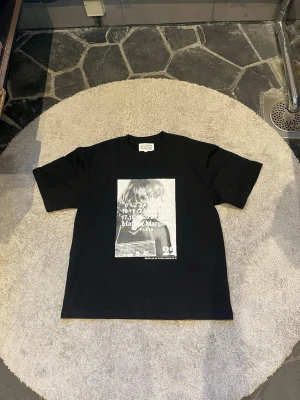Svart t-shirt Maison Margiela print - Cool svart t-shirt från Maison Margiela med stort grafiskt print i vitt och grått framtill. Klassisk passform med korta ärmar och rund hals. Tillverkad i mjuk bomull som känns skön mot huden. Perfekt för dig som gillar streetwear och statement-plagg.