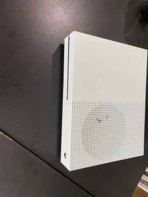 Xbox One S vit spelkonsol med El kabel, ingen handkontroll med, funkar bra - Säljer en Xbox One S spelkonsol i snygg vit färg med stilren design. Konsolen har ventilerad framsida och flera anslutningar på baksidan, inklusive HDMI, USB och nätverksport. Perfekt för gaming och streaming hemma.