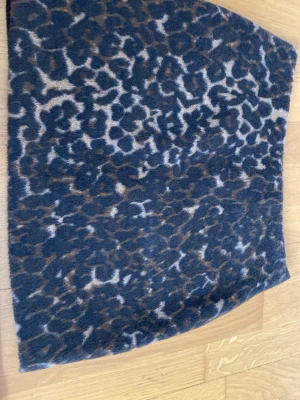 Leopardmönstrad kortkjol i ull - Snygg kortkjol med leopardmönster i mörkblått och brunt. Kjolen har en rak och enkel form som är lätt att matcha med olika toppar. Materialet är mjukt och känns lyxigt tack vare ullblandningen. Perfekt för dig som vill ha en trendig look med lite edge.