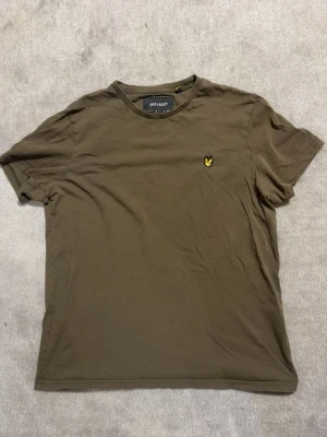 Lyle & Scott T-shirt olivgrön – Strl M - Säljer en stilren Lyle & Scott T-shirt i olivgrön färg med broderad logga på bröstet. Enkel och snygg modell som passar till allt. Fint skick.  📏 Storlek: M ✅ Original Lyle & Scott ✅ Fint skick ✅ Broderad logga ✅ Bekväm passform