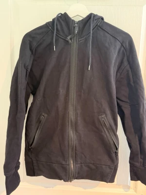 C.P company zip hoodie  - Säljer en svart hoodie i märket c.p company med dragkedja framtill och två fickor med dragkedja. Hoodien har justerbar huva med snören och ribbade muddar vid ärmslut och nederkant. Perfekt för en avslappnad och stilren look. Knappt använd endast legat i garderoben. 