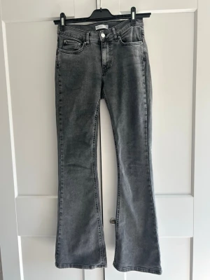 Grå bootcut jeans från Gina Tricot - Säljer ett par grå bootcut jeans från Gina Tricot med hög midja och klassisk femficksmodell. Jeansen har en snygg tvättad look och utsvängda ben. Perfekta för dig som gillar en trendig och avslappnad stil.