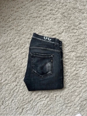 Svarta jeans från dondup  - Säljer ett par svarta jeans från dondup med slitningar och distressed detaljer på benen. Jeansen har klassisk femficksmodell, låg midja och är tillverkade i stretchigt denimtyg för en bekväm och snygg passform. Om du har några frågor är det bara att höra av dig😊