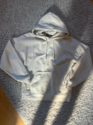 Beige hoodie med huva - Lätt oversized beige hoodie från bikbok med stor huva och dragsnören. Hoodien har en rymlig magficka och ribbade muddar vid ärmslut och nederkant. Tillverkad i mjukt bomullsmaterial som känns skönt mot huden. Perfekt för en avslappnad och stilren look. Superskön men säljer tyvärr då den ej kommer till användning 💕