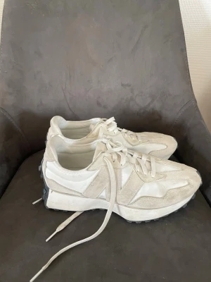 Vita New Balance 327 sneakers - Säljer ett par vita New Balance 327 sneakers med beige mockadetaljer och vita meshpaneler. Skorna har en chunky sula med svarta gummidetaljer baktill och klassisk snörning. Perfekta för dig som gillar stilrena och sportiga sneakers.