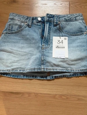Ljusblå denimskort - Trendigt ljusblå denimskort med klassisk femficksdesign, rå kant nertill och knappgylf. Skorten har en avslappnad passform och är tillverkad i 100% bomull. Perfekt för dig som gillar en cool och avslappnad stil.