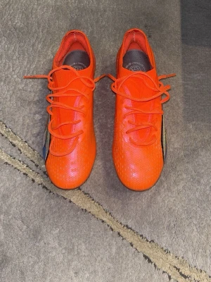 Orangea Puma fotbollsskor - Säljer ett par grymt snygga orangea fotbollsskor från Puma. Skorna har klassisk låg profil, snörning och den ikoniska Puma-loggan i svart, vitt och blått på sidan. Ovandelen är i syntetmaterial som ger bra bollkontroll och passform. Perfekta för dig som vill sticka ut på planen!