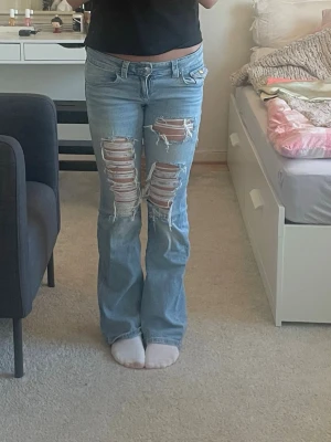 Ljusblå slitna bootcut jeans - Ett par lågmidjade ljusblå jeans från Gina Tricot som jag har gjort massa hål i själv. De är storlek 158. Skriv om ni har frågor!💙