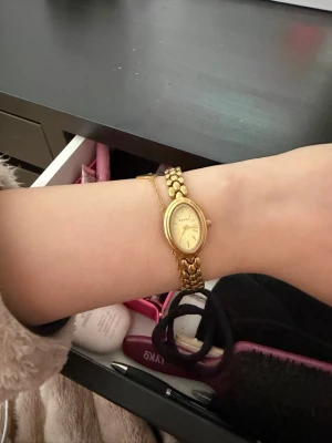 Guldig BOVOU damklocka med länkarmband - Snygg guldig klocka från BOVOU med ovalt ur och länkarmband i metall. Klockan har en stilren design med diskret logga på urtavlan och passar perfekt för dig som gillar klassiska accessoarer med lite lyxig känsla.
