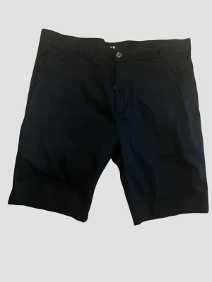 Mörkblå shorts från H&M (52) - Snygga mörkblå shorts från H&M i storlek 52 (motsvarar L i verkligheten)  med klassisk passform. De har knapp och dragkedja framtill samt två bakfickor med knapp. Perfekta för sommaren och tillverkade i mjuk bomull för skön känsla.