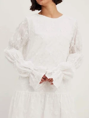 Vit spetsklänning med volangärmar - Superfin vit kortklänning med broderade blommor och volangärmar. Klänningen har öppen rygg med knyt och är tillverkad i ett lätt, luftigt material. Perfekt för sommarens alla tillfällen och ger en romantisk vibe.