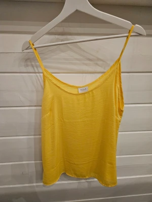 Gul linnetopp från VILA - Snygg gul linnetopp från VILA med tunna axelband och enkel, avslappnad passform. Tillverkad i 100% polyester vilket gör den lätt och skön att bära. Perfekt för varma dagar och enkel att styla med olika outfits.