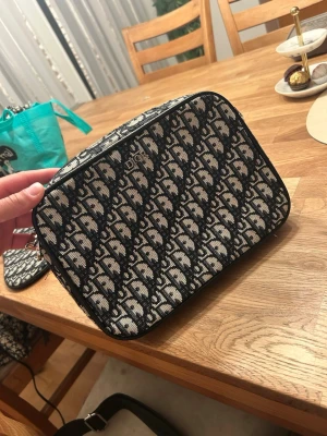 Svart och Beige handväska  - Snygg handväska i svart och beige canvas med klassiskt monogrammönster. Väskan har en rektangulär form och dragkedja samt matchande mindre necessär. Perfekt för dig som gillar lyxiga accessoarer och vill sticka ut med en ikonisk design.