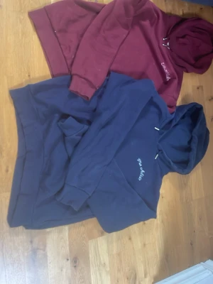 Två hoodies Ma Chérie & Essentials - Säljer två hoodies, en marinblå med broderad text 'Ma Chérie' och en vinröd med texten 'Essentials'. Båda har huva och känguruficka framtill. Perfekta för en chill och avslappnad stil. Mjukt material och klassisk passform.Ska naturligtvis tvättas.PRIS KAN DISKUTERAS‼️