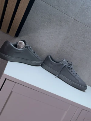 Gråa Oliver Cabell lädersneakers - Stilrena gråa sneakers från Oliver Cabell i slät italiensk läder. Klassisk låg modell med matchande grå skosnören och diskret design utan synliga loggor på utsidan. Perfekta för dig som gillar minimalistisk och clean stil.