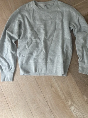 Grå sweatshirt från Uniqlo, Crewneck - Klassisk grå sweatshirt från Uniqlo i mjuk bomull. Tröjan har rund halsringning, ribbade muddar vid ärmslut och nederkant samt en diskret detaljsöm vid halsen. Perfekt basplagg för en avslappnad stil.