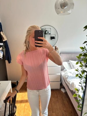 Rosa plisserad topp med kort ärm - Säljer en ljusrosa topp med plisserad struktur och korta ärmar. Toppen har en rak passform och rund halsringning. Perfekt för dig som gillar en enkel men ändå trendig stil.