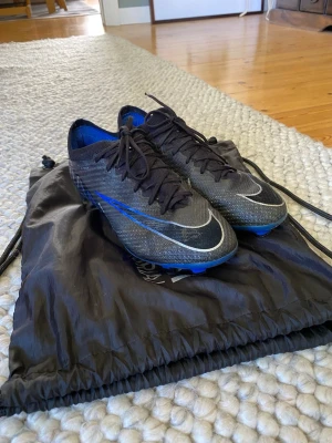 Nike Air Zoom Mercurial vapor 15 - Säljer ett par Nike Mercurial fotbollsskor i svart med blå och vita detaljer. Använda i en halv säsong, mestadels på gräs.