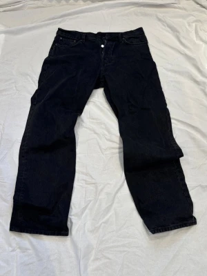 Svarta raka jeans weekday  - Säljer ett par svarta jeans med rak passform och klassisk femficksdesign. Jeansen har knappgylf och är tillverkade i ett kraftigt denimtyg. Perfekta för dig som gillar en enkel och stilren look.