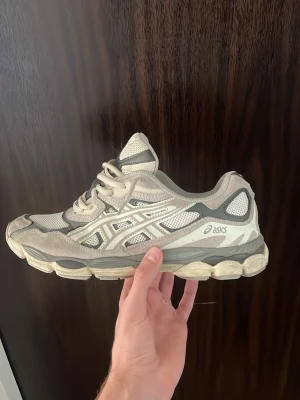 Asics GEL NYC beige sneakers - Snygga Asics GEL-1130 sneakers i beige och grå toner med mesh och mockadetaljer. Skorna har en chunky sula och klassisk Asics-logga på sidan. Perfekta för dig som gillar retrostil och bekväma sneakers med sportig vibe.