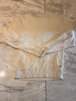 Beige strukturerad sweatshirt - Säljer en beige sweatshirt med strukturerat mönster och rund hals. Tröjan har långa ärmar och ribbade muddar vid ärmslut och nederkant. Perfekt för dig som gillar en enkel men ändå stilren look.