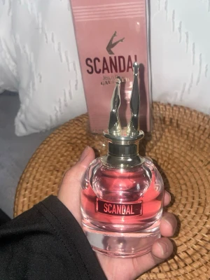 Scandal parfym från Jean Paul Gaultier - Scandal parfym från Jean Paul Gaultier med en unik flaska i glas och en rosa doftvätska. Flaskan har ett coolt lock i form av guldfärgade ben och etikett med loggan. Förpackningen är rosa med metallicdetaljer och tydlig branding.