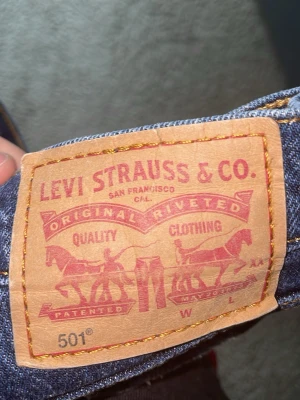 Levi's 501 raka blå jeans - Klassiska blå Levi's 501 jeans med rak passform och fem fickor. Jeansen har den ikoniska läderpatchen bak i midjan och kontrastsömmar. Tillverkade i slitstark denim, perfekta för en avslappnad och tidlös stil. De är rätt så små de har krympt i tvätten också och jag har växt mycket. De passar 11 12 13 14 åringar kanske beroende på hur långa ni är och så. De står ingen storlek i dom tyvärr men man jag vet ungefär. 