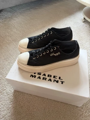 Svarta Isabel Marant sneakers - Snygga svarta sneakers från Isabel Marant med vit tå och tjock vit sula. Skorna har klassisk låg modell, svarta skosnören och metallfärgade öljetter. Märkets logga syns på sidan och under skon på sulan. Tillverkade i canvasmaterial för en avslappnad och trendig look. Skorna är i mycket bra skick!💗