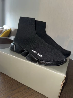Svarta Balenciaga Speed sneakers - Svarta Balenciaga Speed sneakers med stickad ovandel i stretchigt tyg och chunky sula. Diskret vit logga på sidan och futuristisk design. Skorna har en strumpliknande passform och är helt svarta med svart sula.