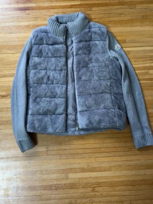 Grå teddyjacka från Moncler - Snygg grå teddyjacka från Moncler med quiltad, fluffig framsida och baksida samt stickade ärmar och krage. Dragkedja framtill och Moncler-logga på ärmen. Perfekt för dig som vill ha en trendig och mysig jacka i höst och vinter. Påse medföljer!😊