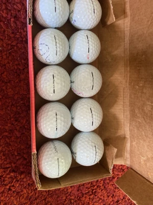 10st Titelest Pro V1/V1x A/B Klass BEGAGNADE - Säljer ett gäng vita golfbollar av modellen Titleist Pro V1 i en öppen kartong. Bollarna har klassisk rund form och vissa har märkningar med svart text och linjer. Perfekt för dig som vill fylla på golfväskan inför säsongen.