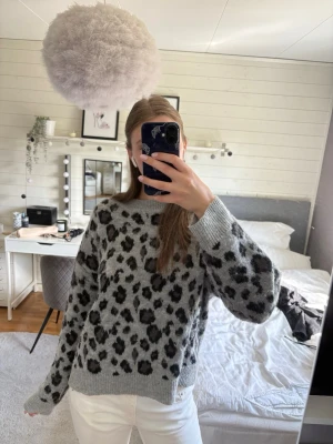 Grå leopardmönstrad stickad tröja - Säljer en grå stickad tröja med svart leopardmönster. Tröjan har rund halsringning och ribbade muddar vid ärmslut och nederkant. Perfekt för dig som gillar djurmönstrat och vill ha en trendig look. Är storlek 48, men passar dig som har 36-38 och vill ha lite baggy.