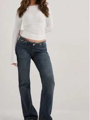 Mörkblå bootcut jeans med låg midja - Snygga mörkblå bootcut jeans med låg midja och klassisk femficksdesign. Jeansen har slitna detaljer vid benslut och är tillverkade i ett mjukt denimtyg med lätt stretch. Perfekta för en avslappnad och trendig look.