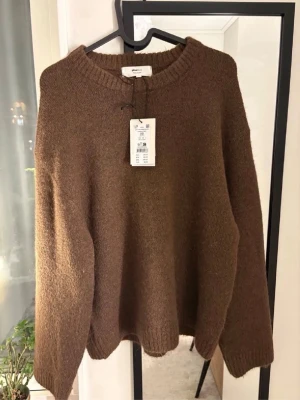 Brun stickad tröja från gina - Mysig brun stickad tröja från Gina med rund halsringning och ribbade muddar vid ärmslut och nederkant. Tröjan har en avslappnad passform och är tillverkad i ett mjukt material som passar perfekt för kyliga dagar.