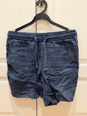 Blå linne shorts med snörning - Snygga mörkblåa linne shorts med elastisk midja och snörning framtill. Shortsen är ifrån A Days March och är i 100% linne. Storlek 46