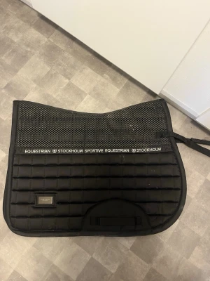 Svart schabrak Equestrian Stockholm - Säljer ett svart schabrak från Equestrian Stockholm med rutmönster och mesh upptill för extra ventilation.