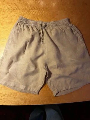 Beige linneshorts med snörning - Snygga och luftiga beige shorts i linne med elastisk midja och snörning framtill. Perfekta för varma dagar och har en avslappnad passform. Två sidofickor för extra funktionalitet. Från gant i storlek 164.