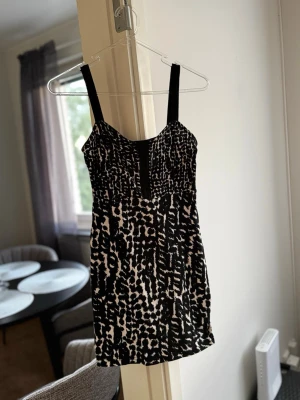 Svartvit leopardmönstrad kort klänning - Snygg kort klänning med svartvita leopardmönster och breda axelband. Klänningen har en markerad byst och korsett framtill för enkel påklädning. Perfekt för dig som vill sticka ut med ett djurmönster. Materialet känns mjukt och följsamt. Passar xs-s