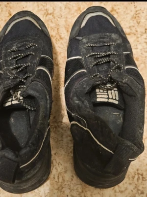 Svarta sneakers med vita detaljer - Snygga svarta sneakers med vita detaljer och reflexliknande ränder. Ovandelen är i mesh och syntetmaterial, med svarta och vita skosnören. Skorna har en sportig look och passar perfekt till streetwear.