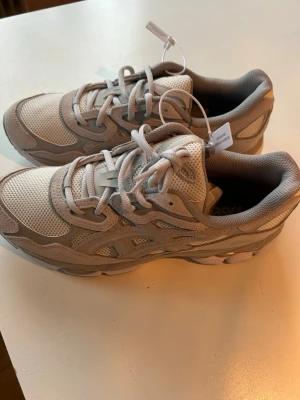 Vita Asics sneakers med mesh och mocka - Säljer ett par fräscha vita Asics sneakers med cool retrostil. Skorna har meshpaneler för bra ventilation och detaljer i mocka och syntet. Tjock sula för skön komfort och klassisk Asics-logga på sidan. Perfekta för dig som gillar sportig och clean look.